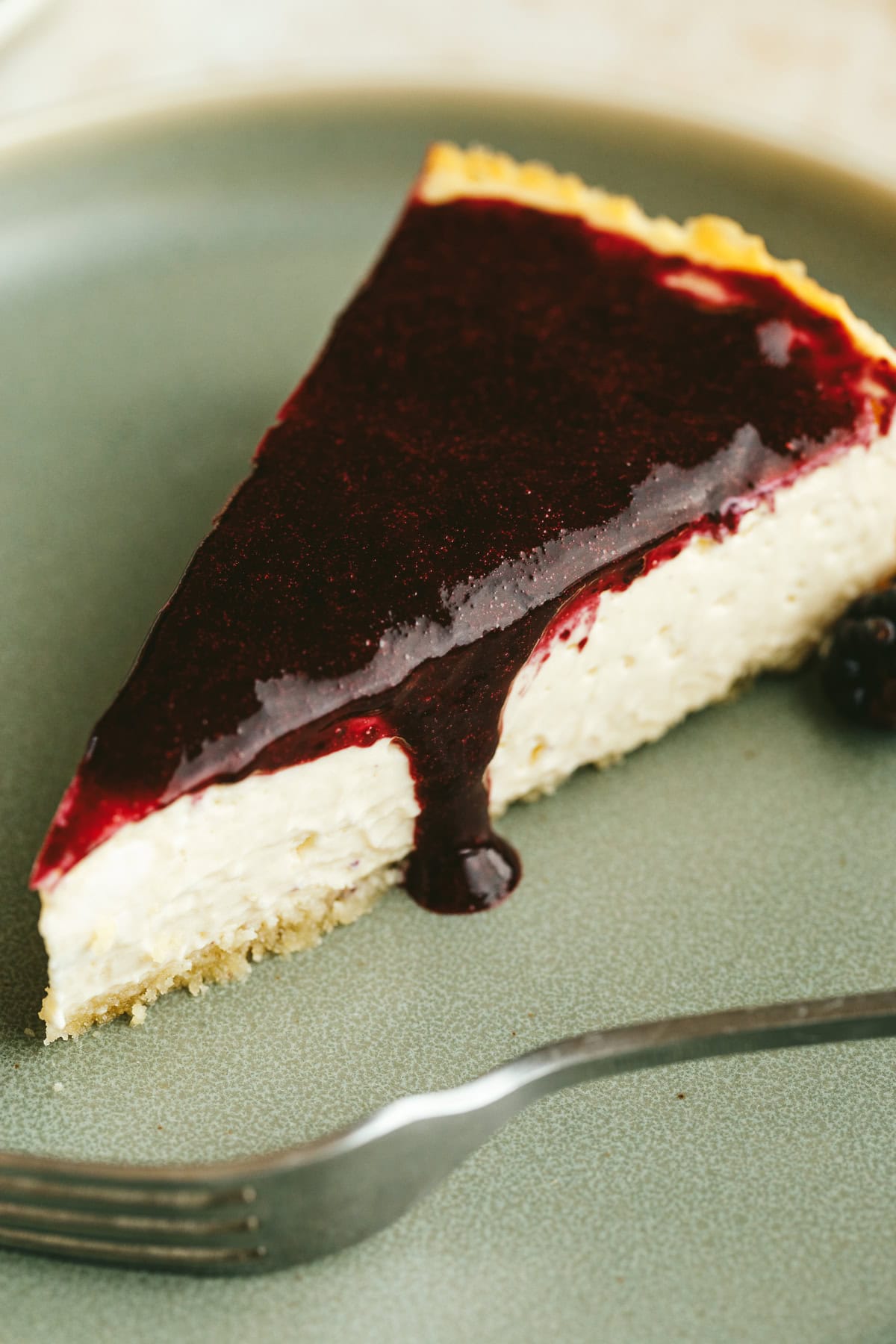 A slice of high protein cheesecake with berry sauce on a plate.