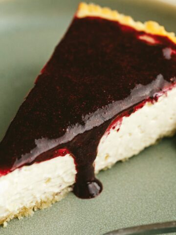 Closeup of a slice of high protein cheesecake with berry sauce.