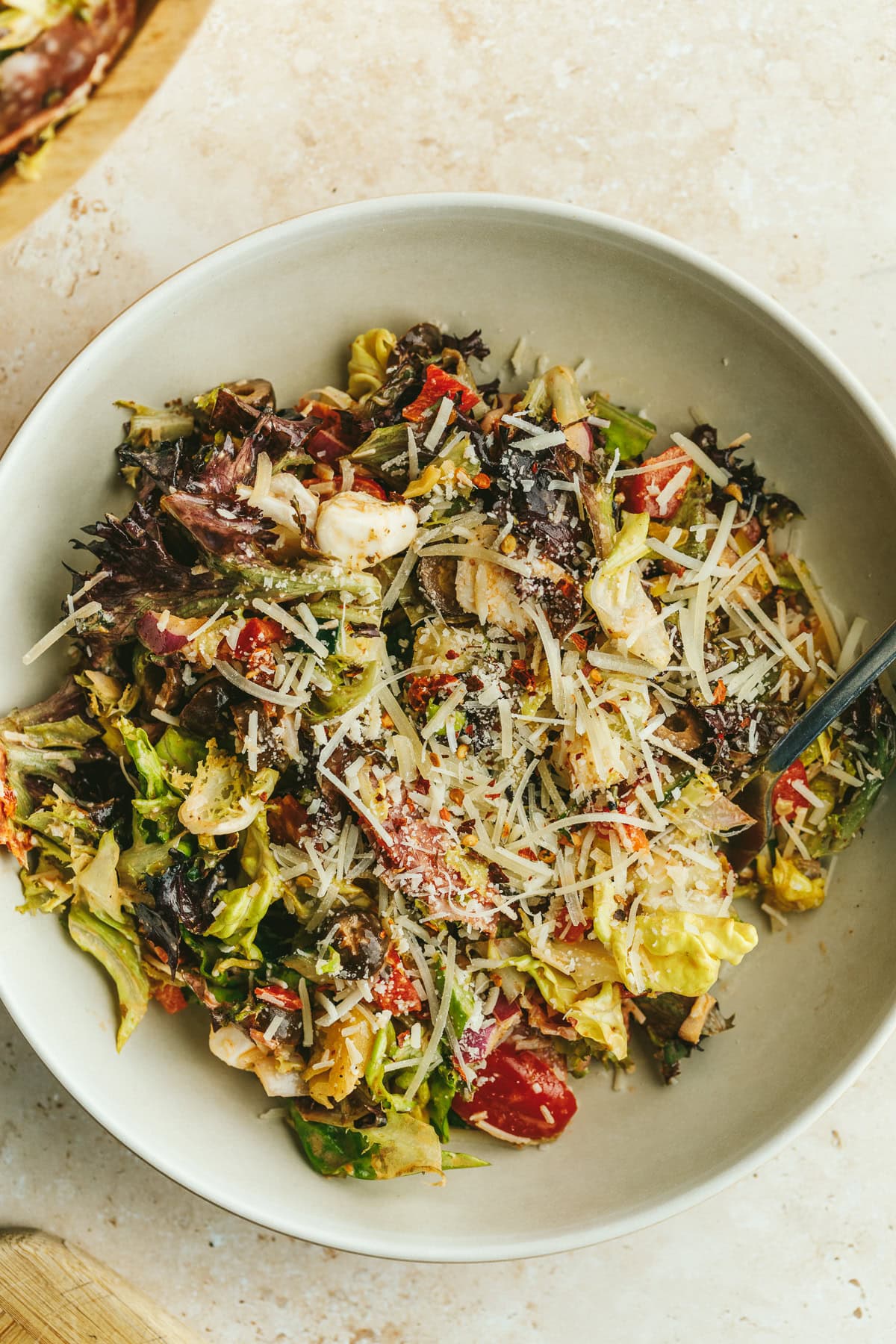 A beige bowl with pizza salad and a fork.