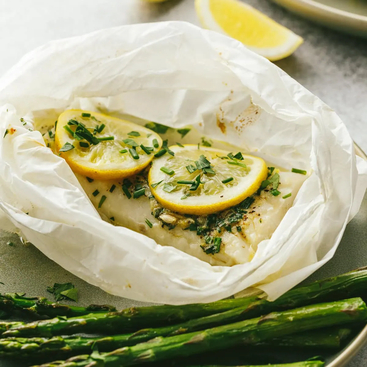 Cod in parchment with lemon slices and parsley on top.
