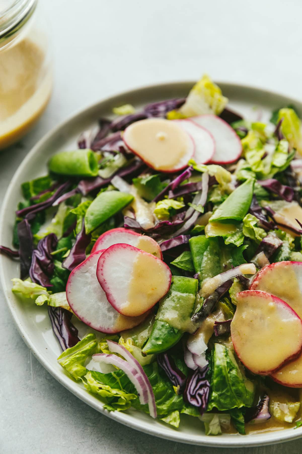 Closeup of a salad with radishes drizzled with lime tahini dressing.