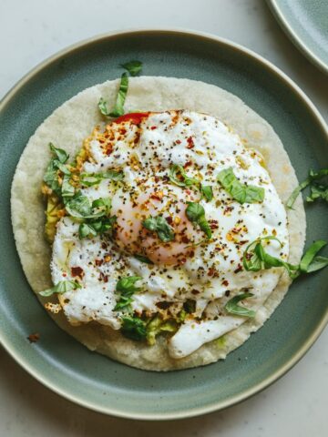 A feta fried egg on a green plate with basil.