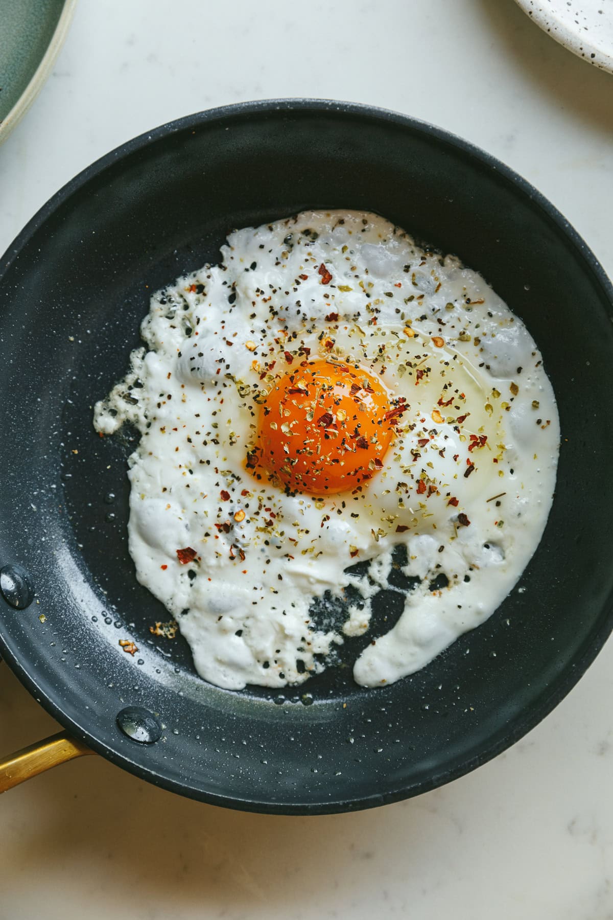A feta fried egg with seasonings in a black pan.