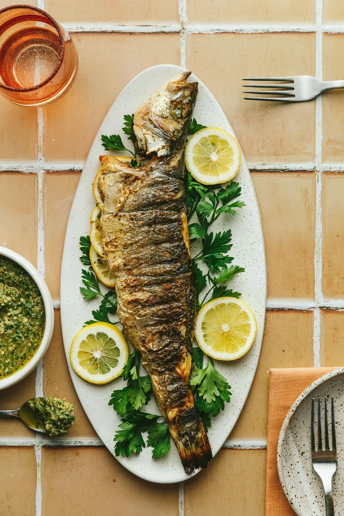 A platter with a whole grilled branzino on top of parsley.