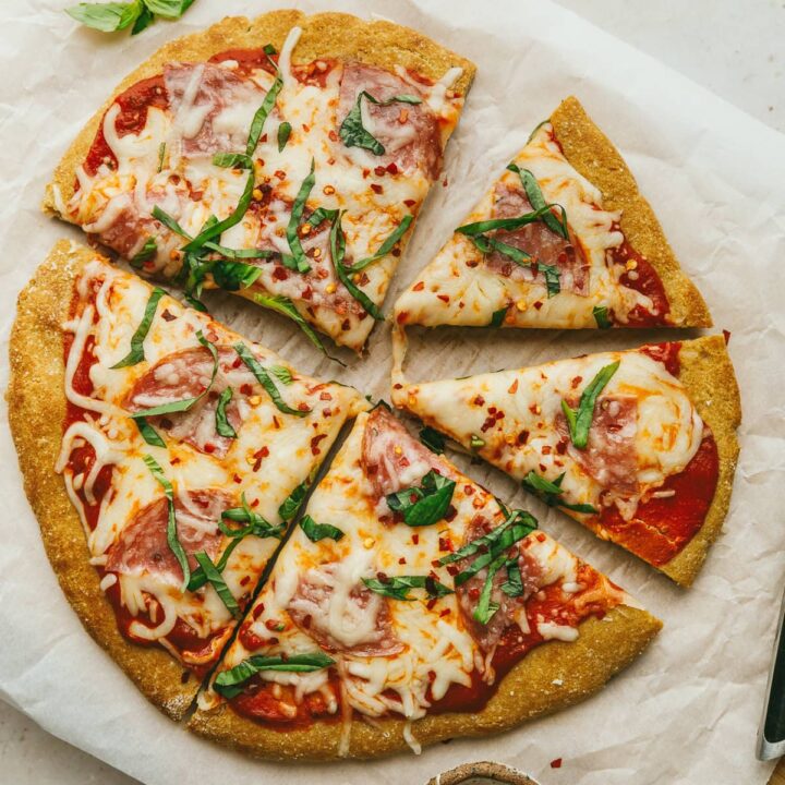 Grain-free pizza crust with fresh basil, cut into slices.
