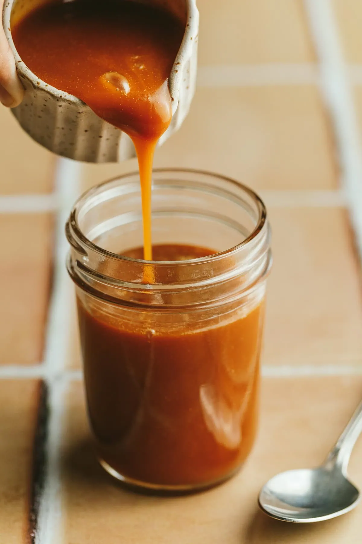 Pouring keto caramel sauce into a glass jar.