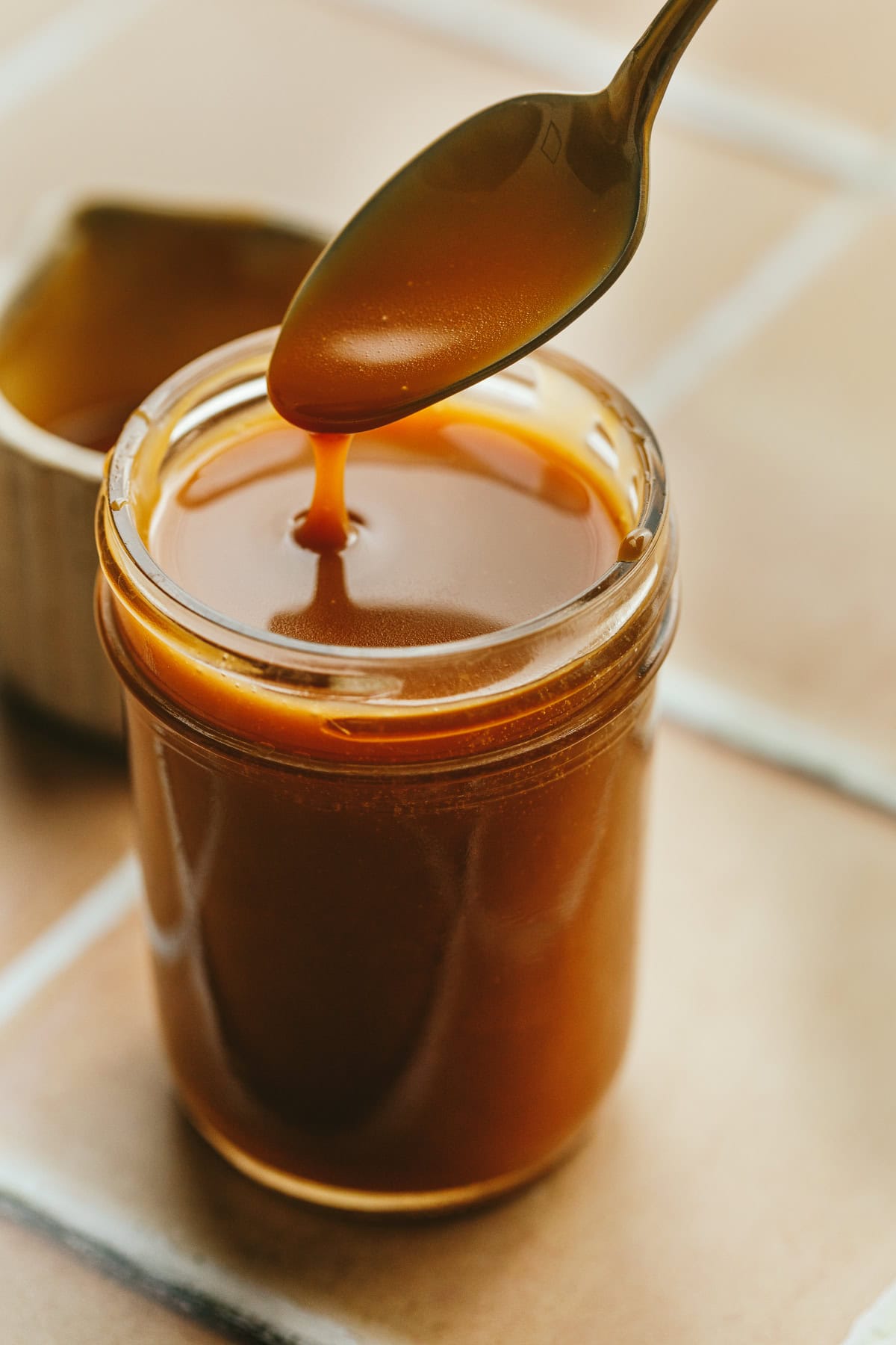 A spoon dripping keto caramel sauce into a glass jar.
