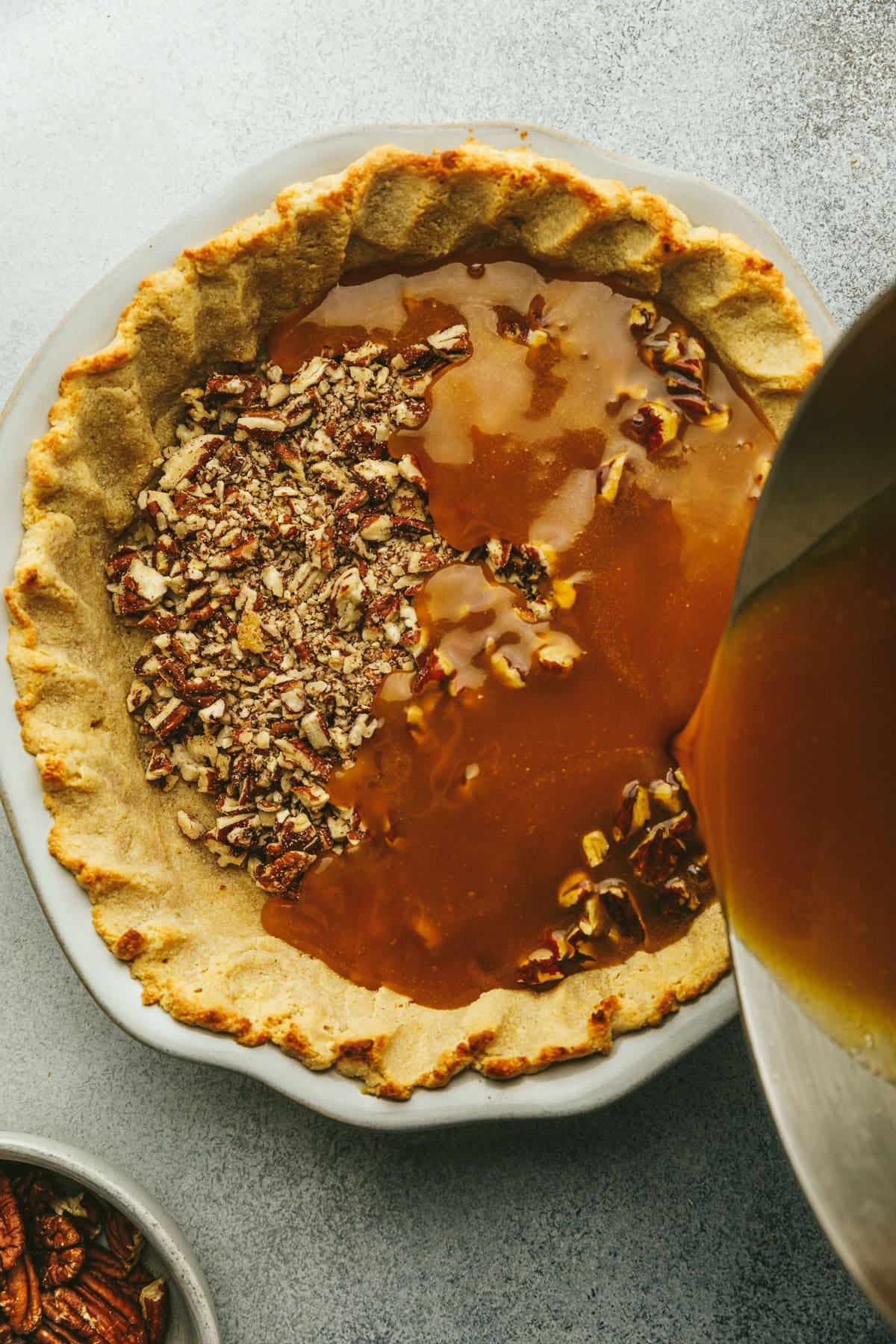 Pouring caramel mixture over chopped pecans into pie crust.