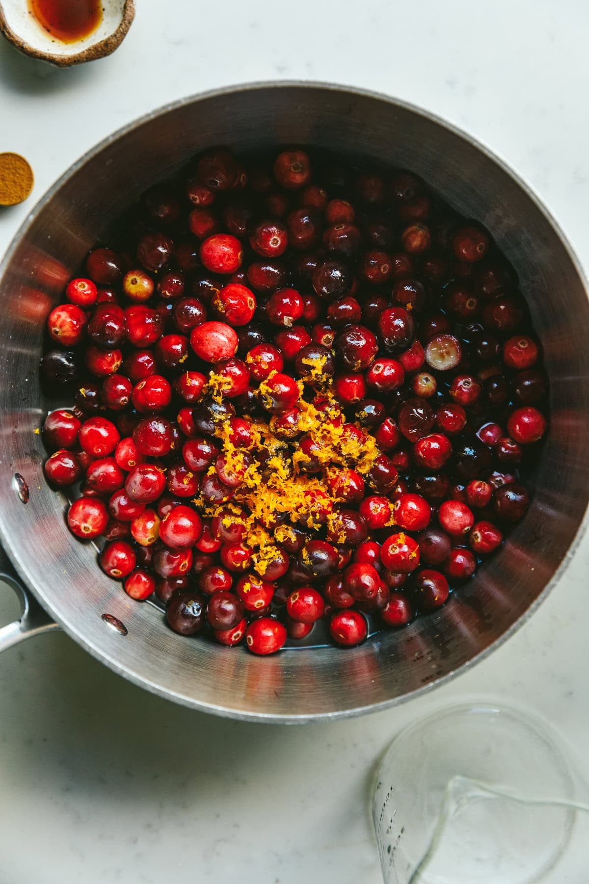 A stainless steel saucepan with whole cranberries and ingredients for sugar-free cranberry sauce.