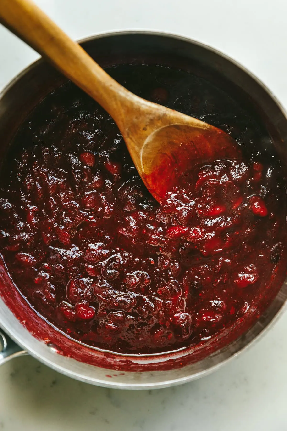 A wooden spoon with keto cranberry sauce in a saucepan.