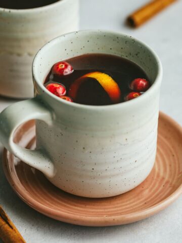 A mug of mulled tea with cranberries, orange peel and cinnamon sticks as garnish.
