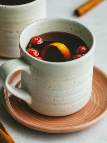 A mug of mulled tea with cranberries, orange peel and cinnamon sticks as garnish.