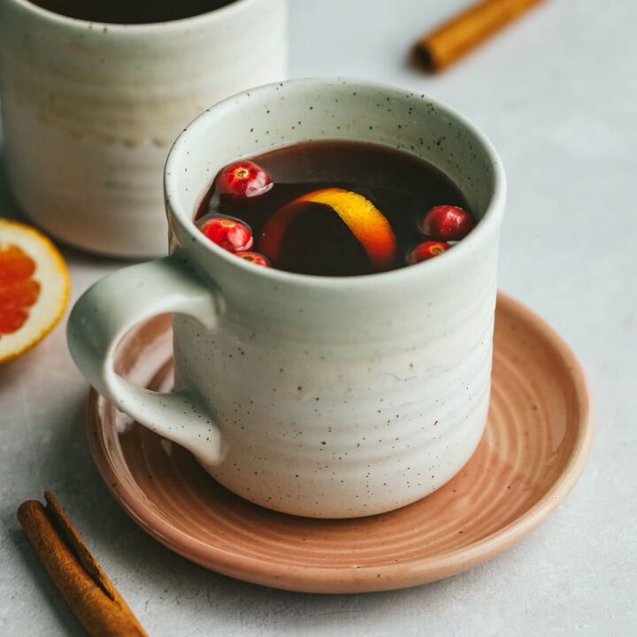A mug of mulled tea with cranberries, orange peel and cinnamon sticks as garnish.