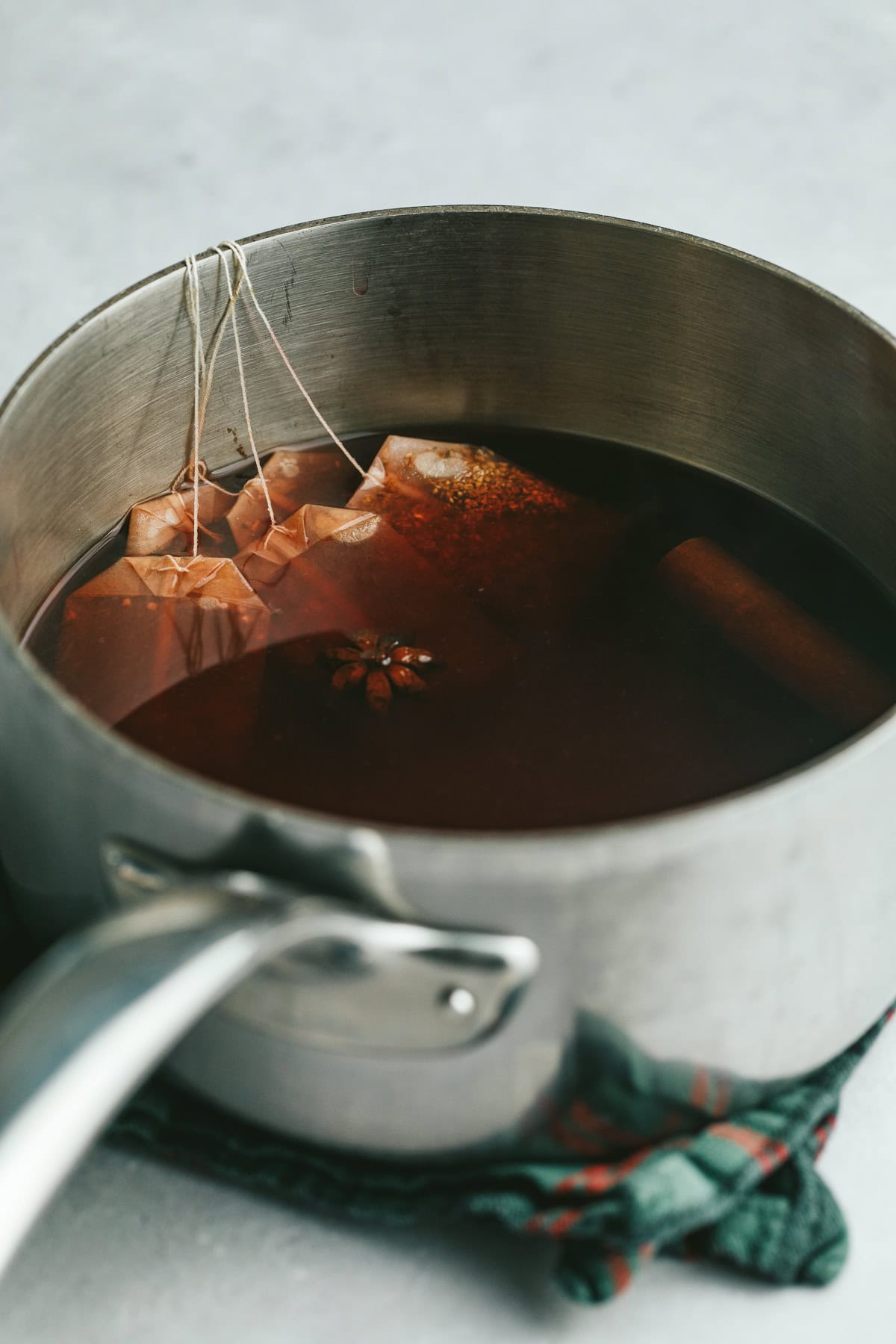 Tea bags steeping in a stainless steel pot of winter spiced mulled tea.