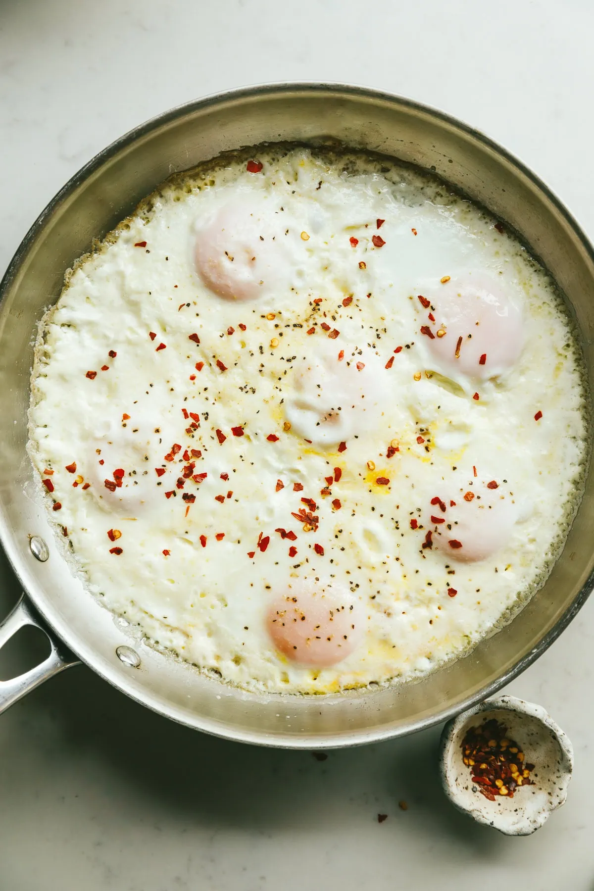 Cooked cream eggs in a stainless steel skillet with red pepper flakes for serving.