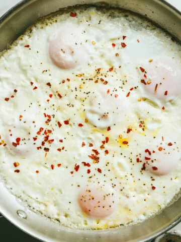 Cream fried eggs in a stainless steel skillet with red pepper flakes.
