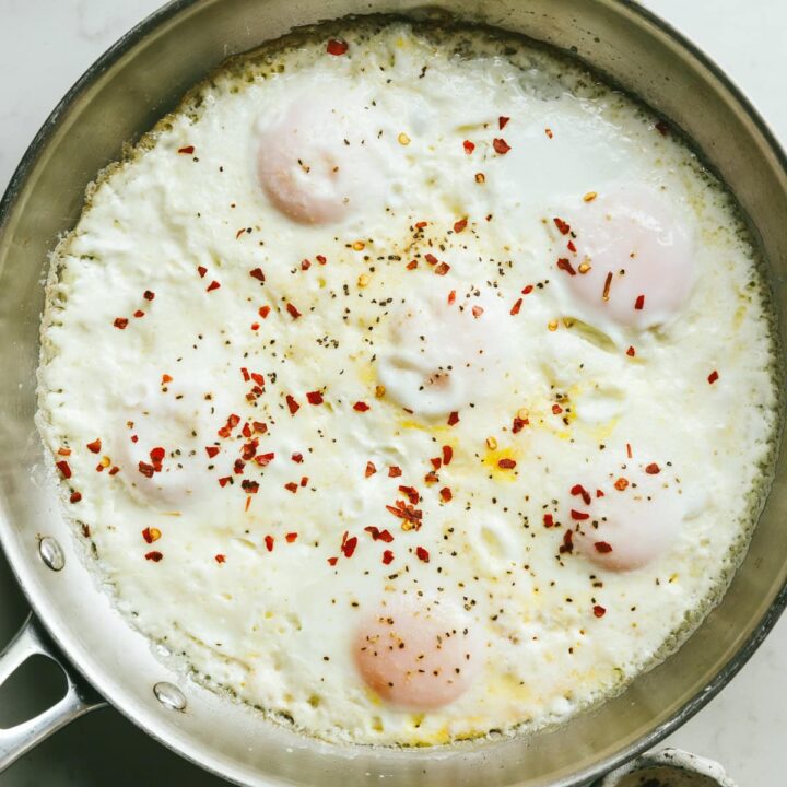 Cream fried eggs in a stainless steel skillet with red pepper flakes.