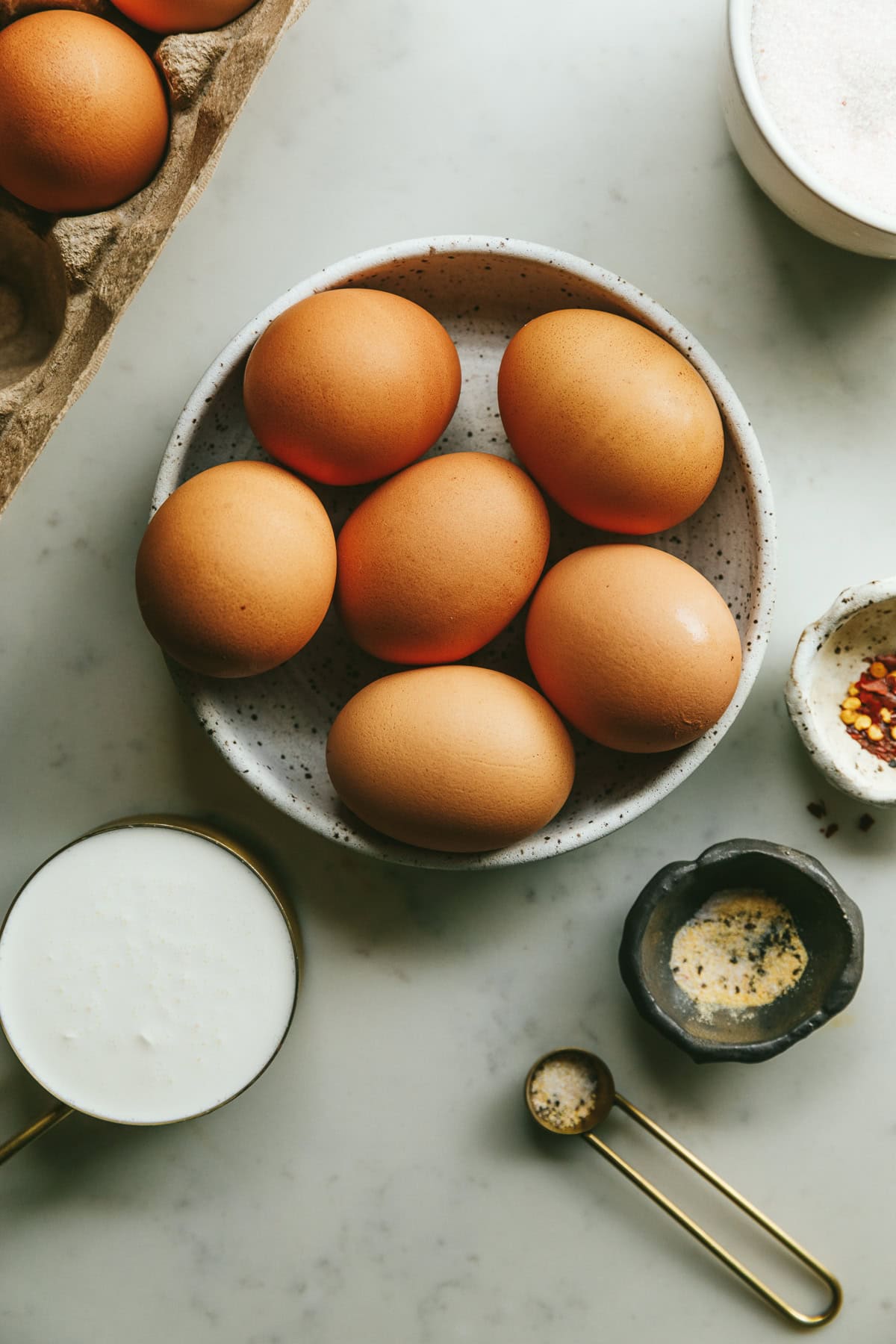 Ingredients for cream fried eggs on a marble counter top, including eggs, seasonings and cream.
