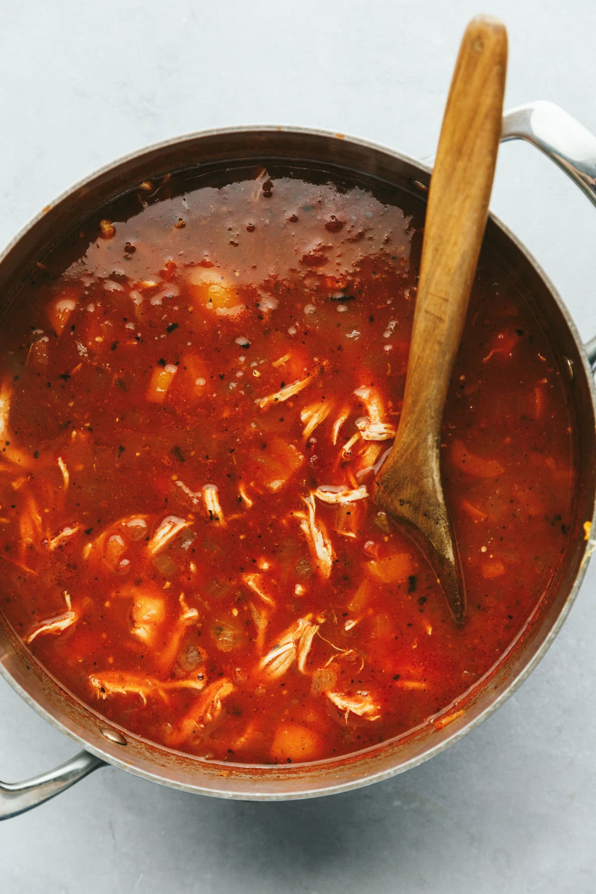 A wooden spoon in a big stainless steel pot of keto chicken tortilla soup.