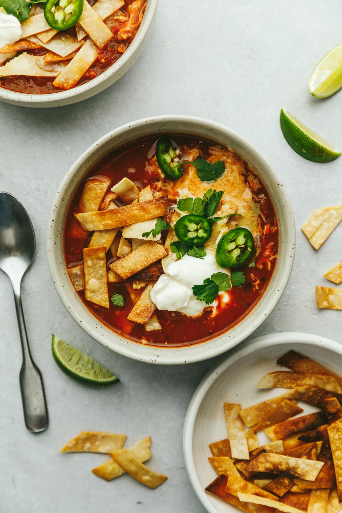 Two bowls of keto chicken tortilla soup with lime wedges and tortilla strips on the side.