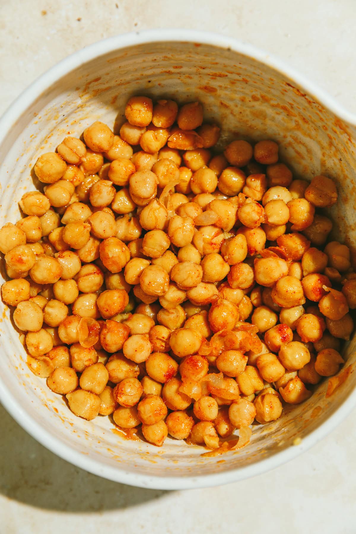 Raw chickpeas tossed in seasonings in a white bowl.