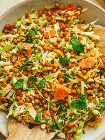 Cabbage crunch salad in a white salad bowl with fresh mint leaves and servingware.