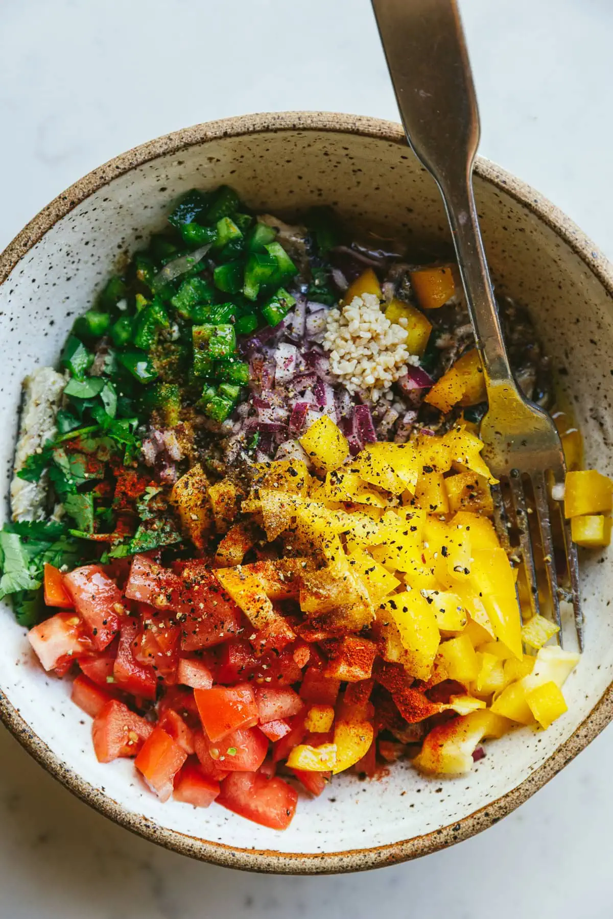 Ingredients for sardine escabeche in a white speckled bowl with a fork.