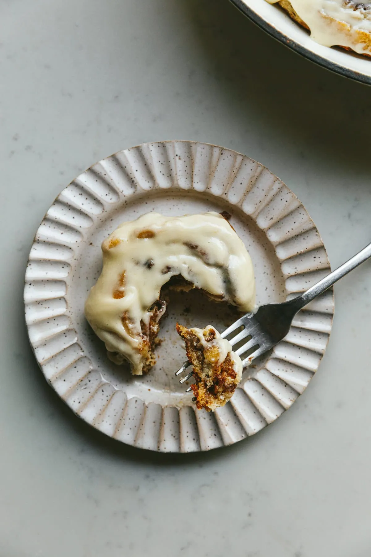 A scalloped plate with a low-carb cinnamon roll and a bite taken out of it.
