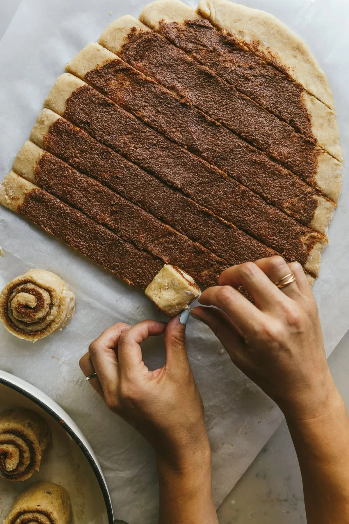 Two hands are rolling each strip of keto cinnamon roll dough to make the cinnamon buns.