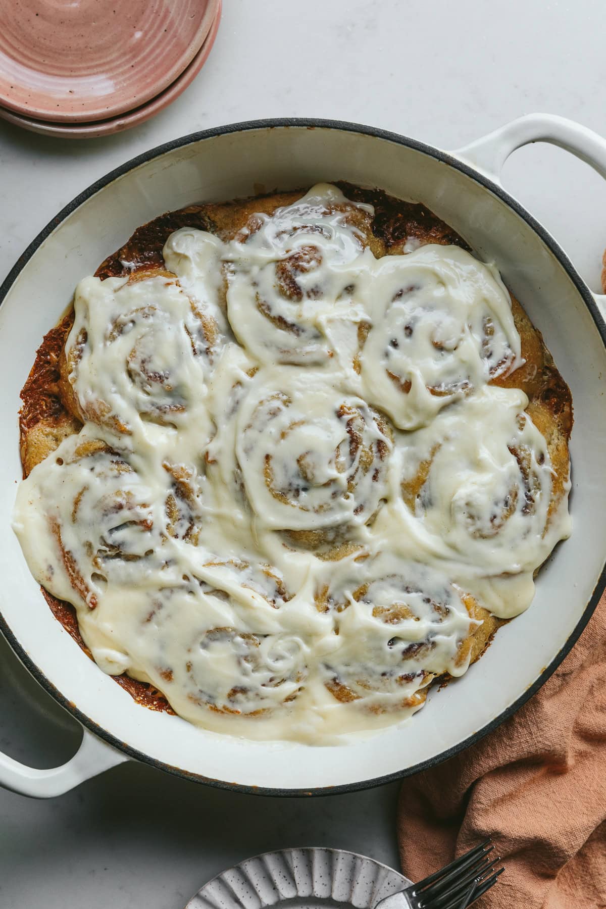 Frosted keto cinnamon rolls in a white baking dish with serving plates next to it.