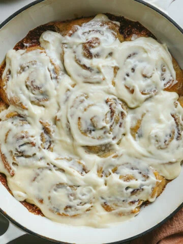 Baked and frosted keto cinnamon rolls in a white braiser dish with a pink napkin next to it.