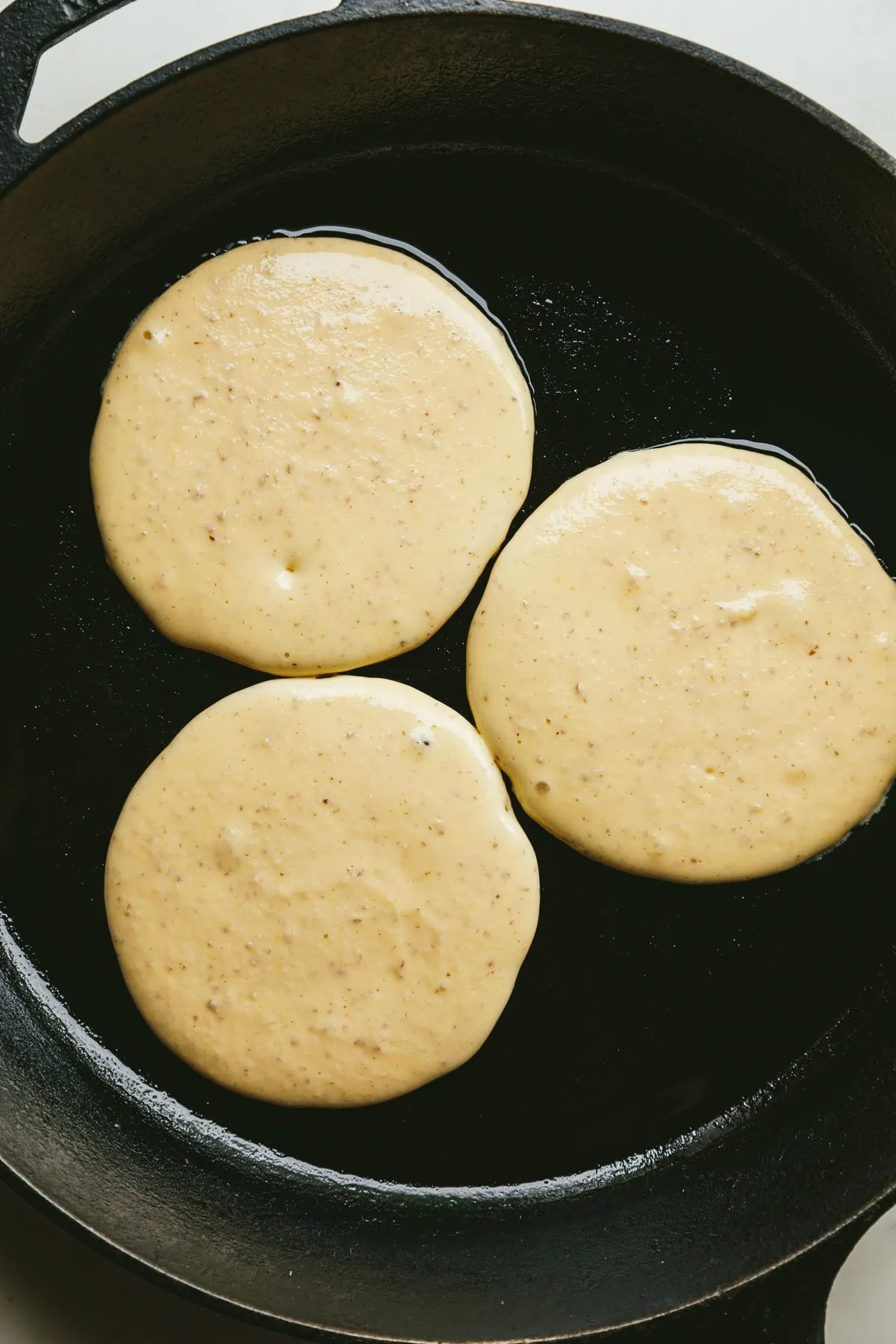 Three low-carb cottage cheese pancakes cooking in a black cast iron skillet.