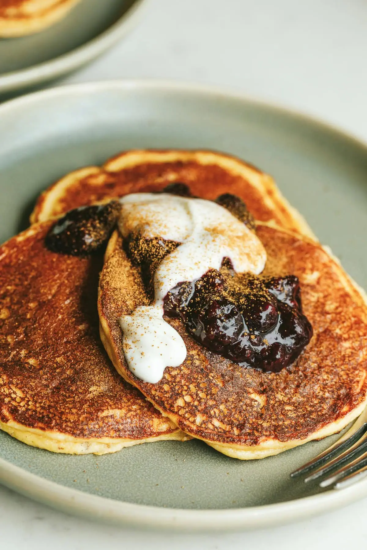 A stack of three low-carb cottage cheese pancakes on a green serving plate with toppings.