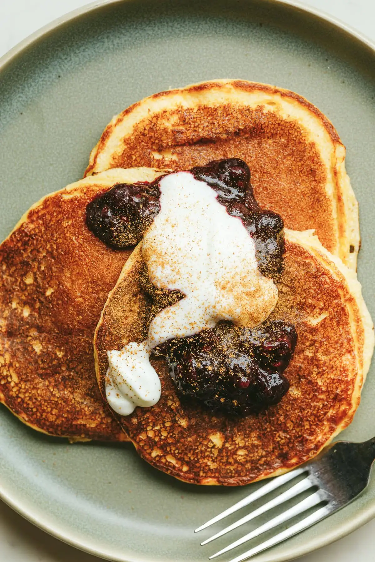 Three keto cottage cheese pancakes on a green plate with berry sauce and yogurt.