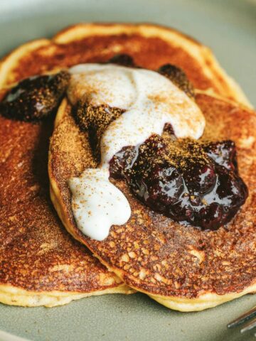 Closeup of three keto cottage cheese pancakes on a serving plate with berry compote, yogurt, and cinnamon.