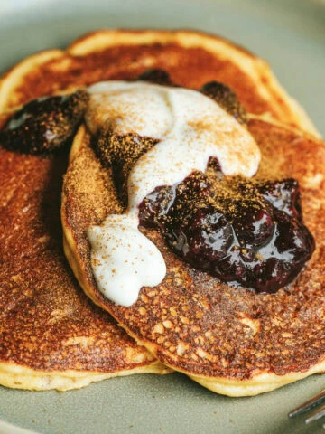 Closeup of three keto cottage cheese pancakes on a serving plate with berry compote, yogurt, and cinnamon.