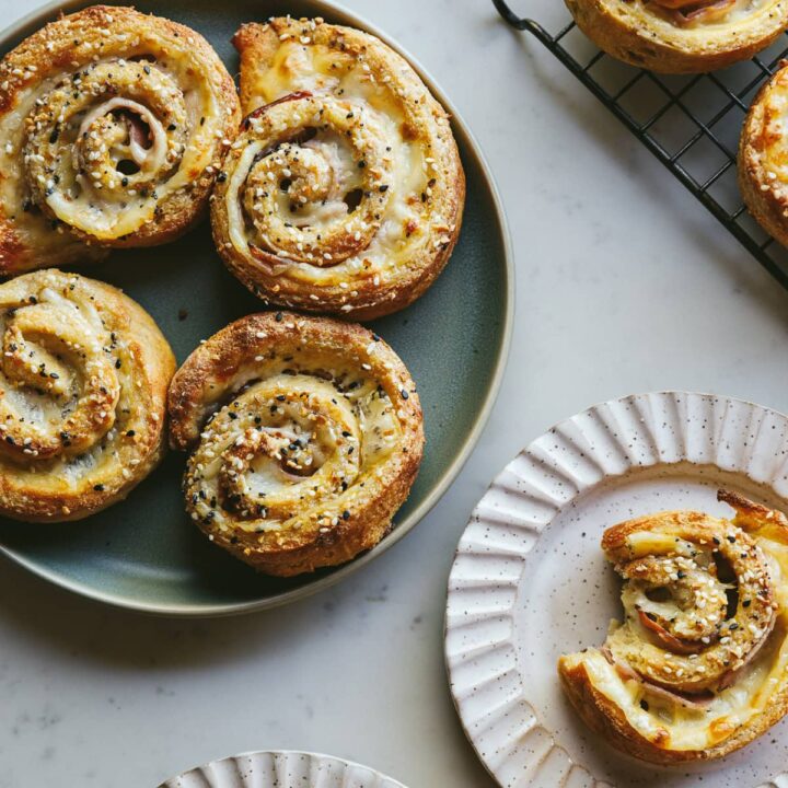 Keto ham and swiss pinwheels on a green plate and white scalloped serving plate.