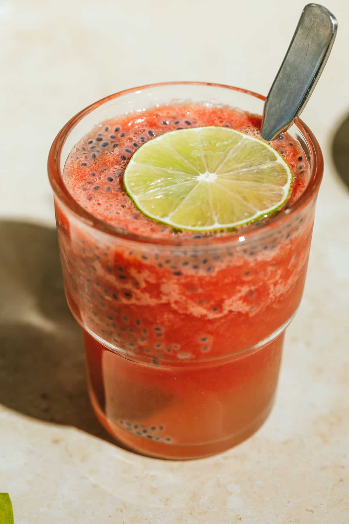 Watermelon slushie basil seed drink with a slice of lime and spoon.