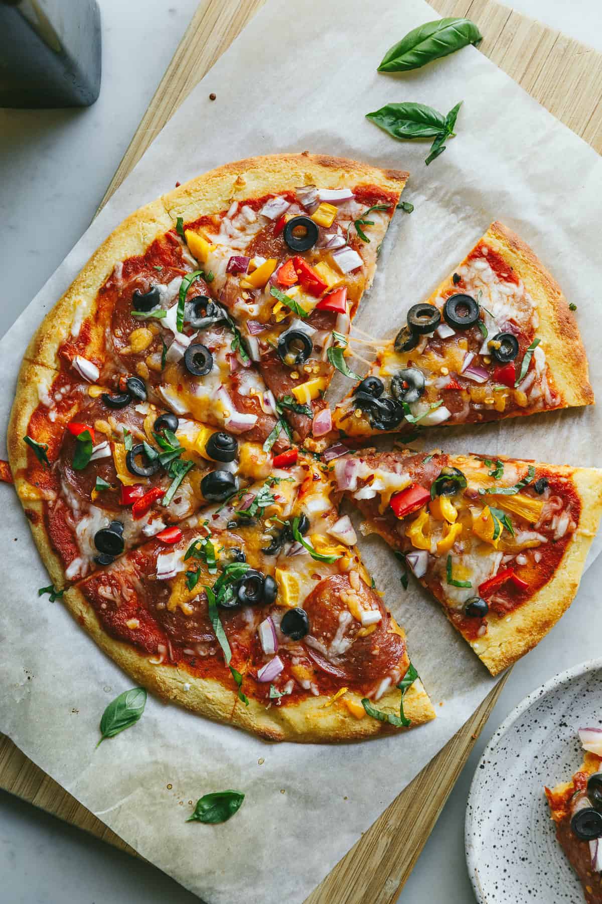 A keto cottage cheese pizza crust loaded with pizza toppings and fresh basil on a cutting board.