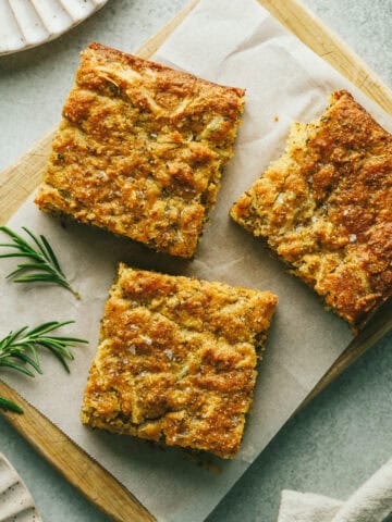 Three slices of a lupin flour bread on a cutting board with fresh rosemary.