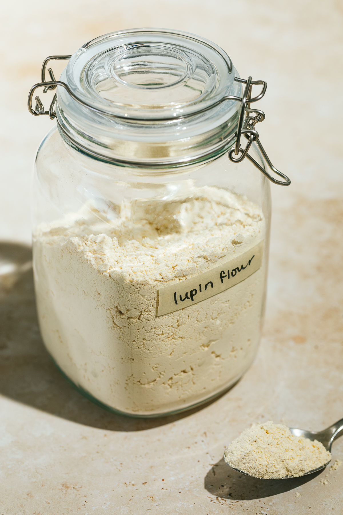 A glass canister with lupin flour and a spoon with flour sitting next to it.