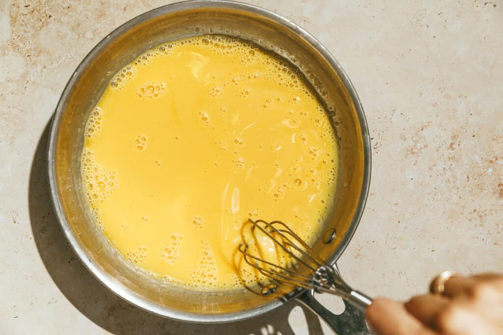 Stirring egg yolks into the cream mixture in a stainless steel pan.
