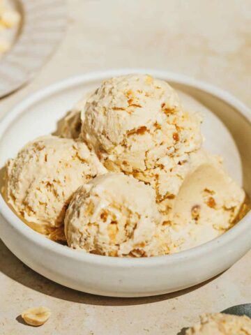 Scoops of keto peanut butter ice cream in a white bowl with peanuts next to it.