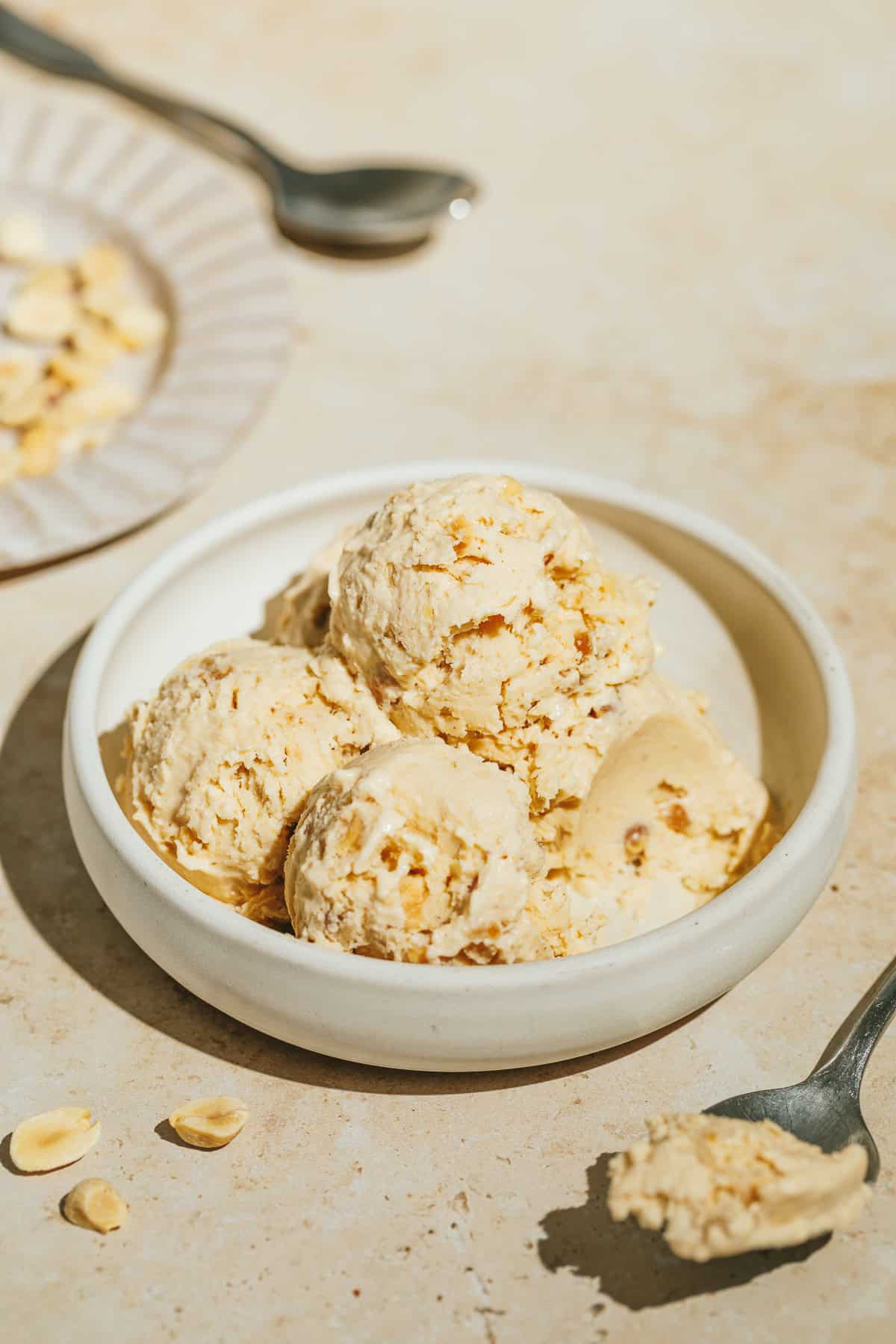 Keto peanut butter ice cream scoops in a white bowl with spoons next to it.