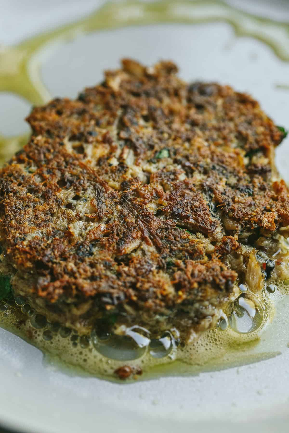 A sardine patty cooking in a skillet.