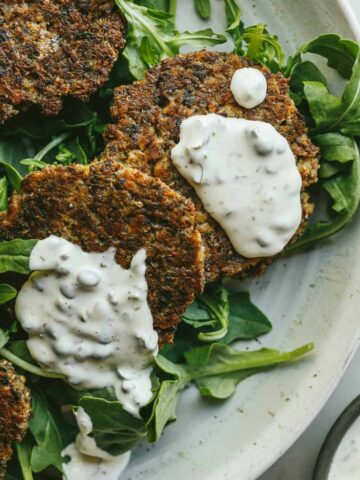 Crispy sardine cakes with caper aioli on greens set on a plate.