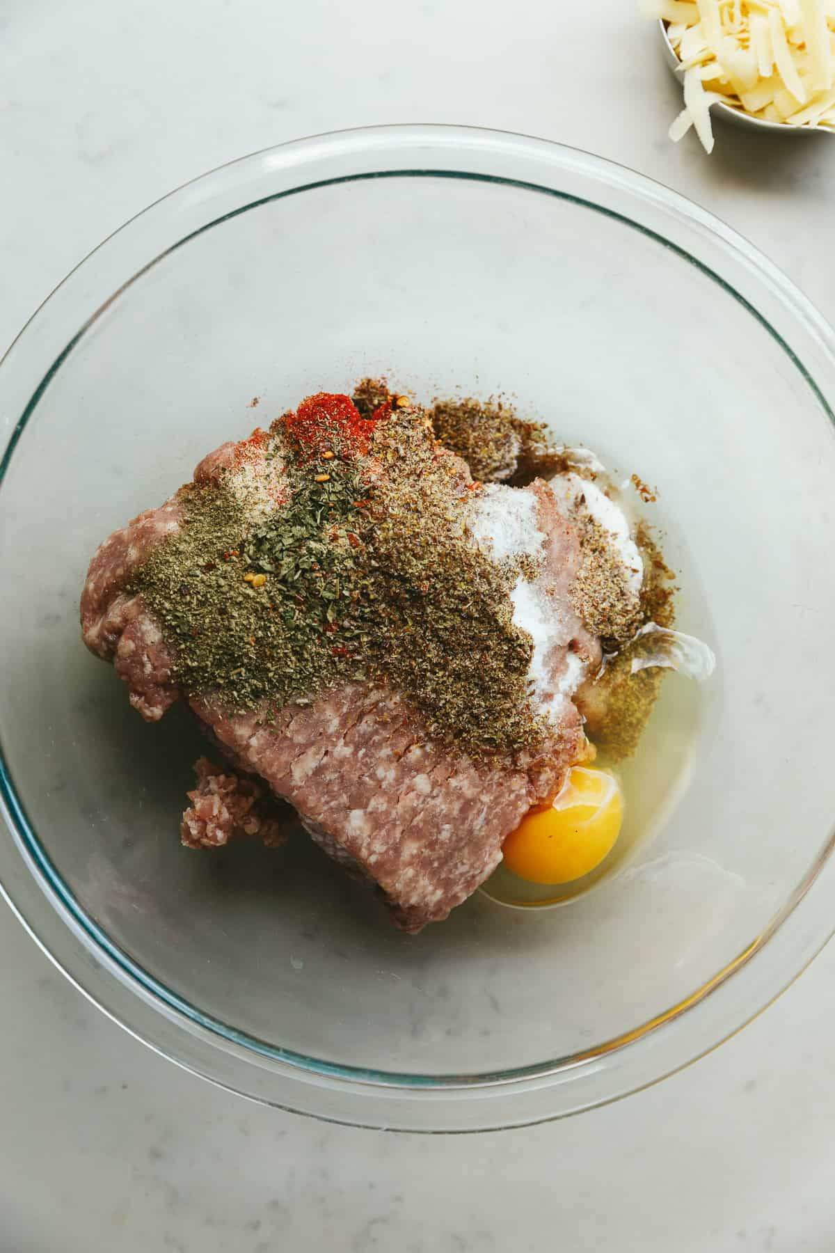 Ingredients for breakfast meatballs in a glass mixing bowl.