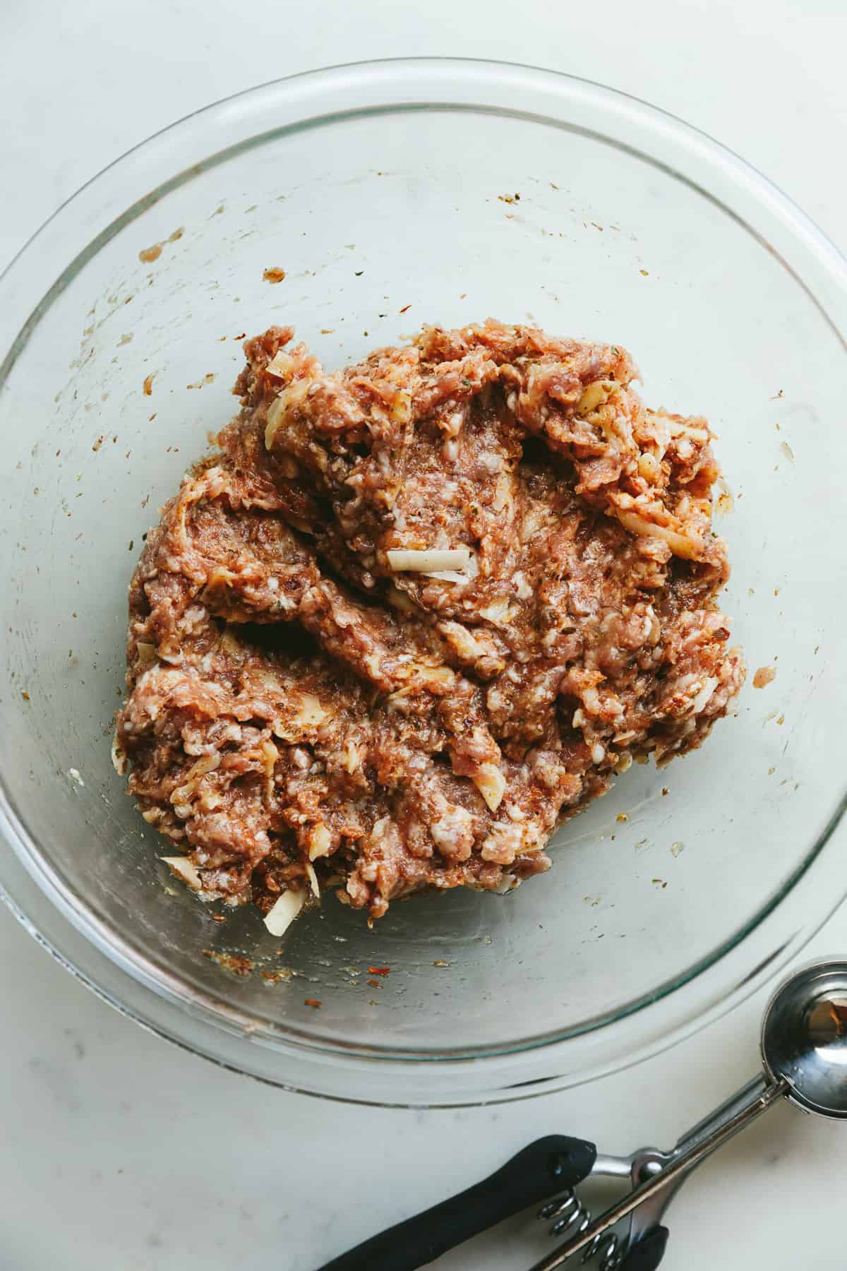 Breakfast meatball mixture in a glass mixing bowl with a cookie scoop next to it.