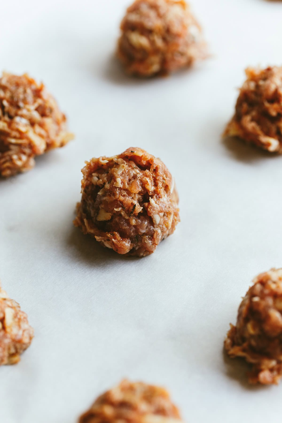 Closeup of unbaked breakfast meatball mixture shaped in a ball on a baking sheet.