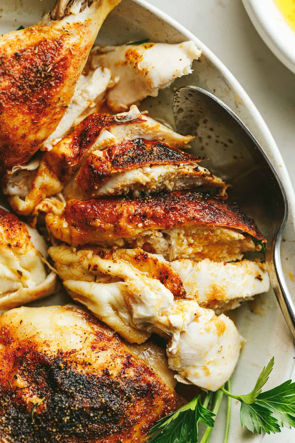 Sliced brown butter chicken on a plate with parsley.